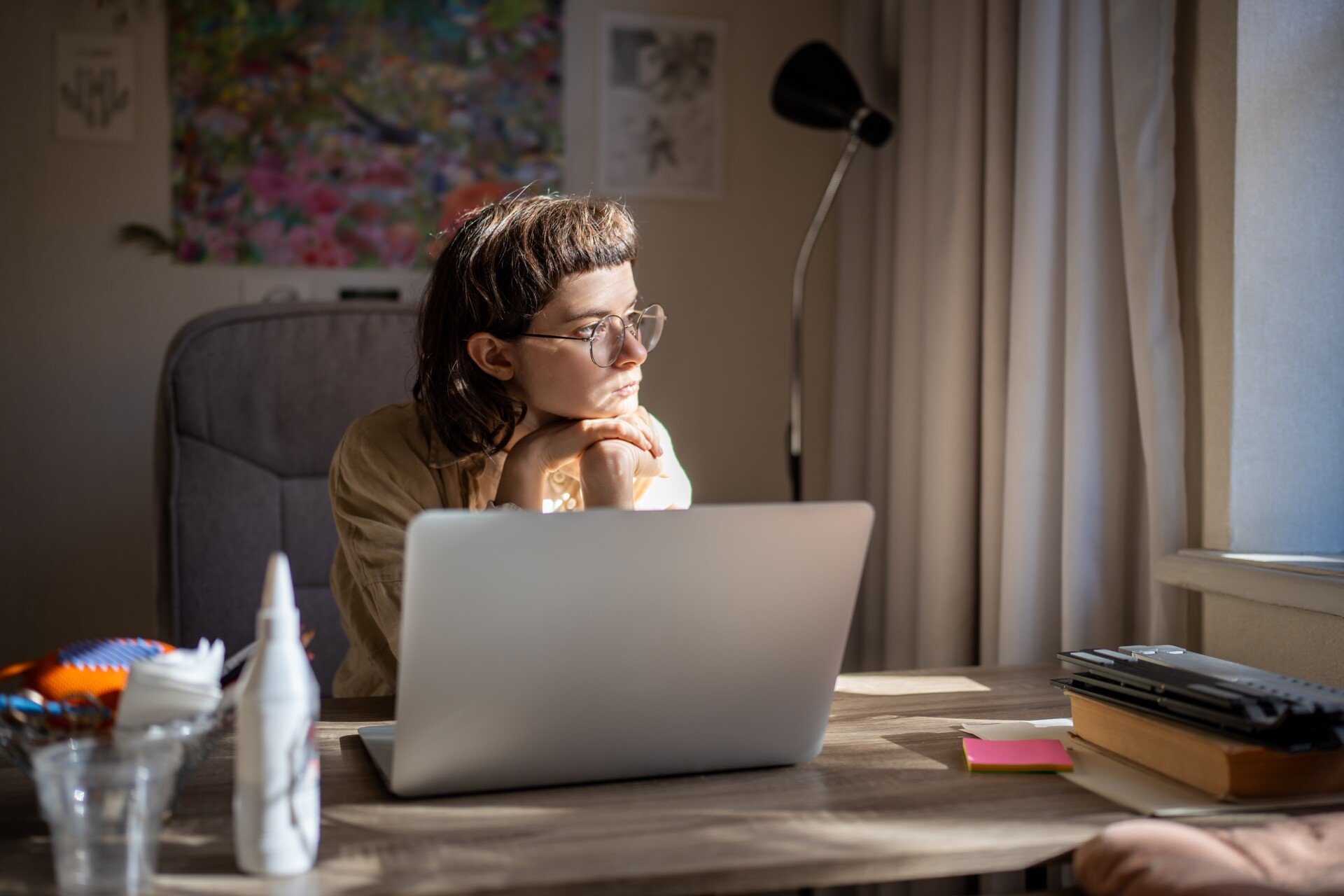 Person sat in front of a laptop procrastinating on work while looking out the window.