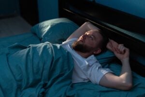 Anxious man lay in bed looking at ceiling.