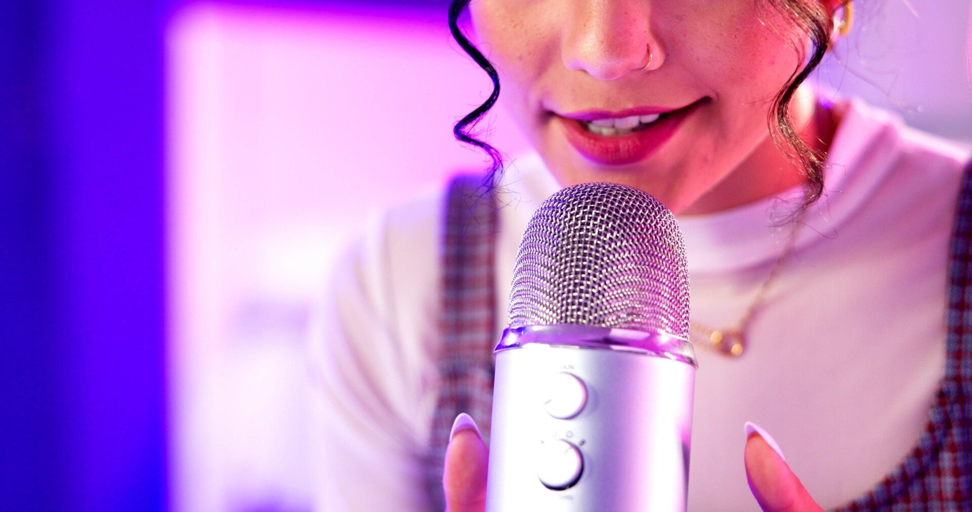 ASMR A close up of a woman speaking softly into a microphone with neon lights in background.