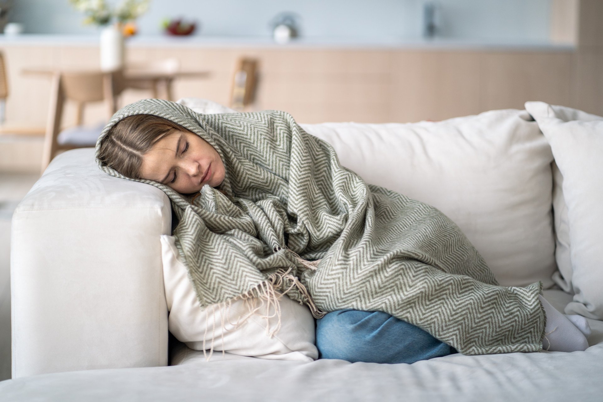 An exhausted woman curled up in a blanket on the sofa.