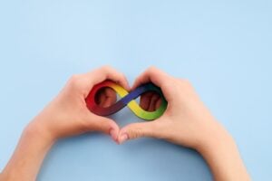 Hands making a heart shape with a rainbow infinity sign inside the heart.