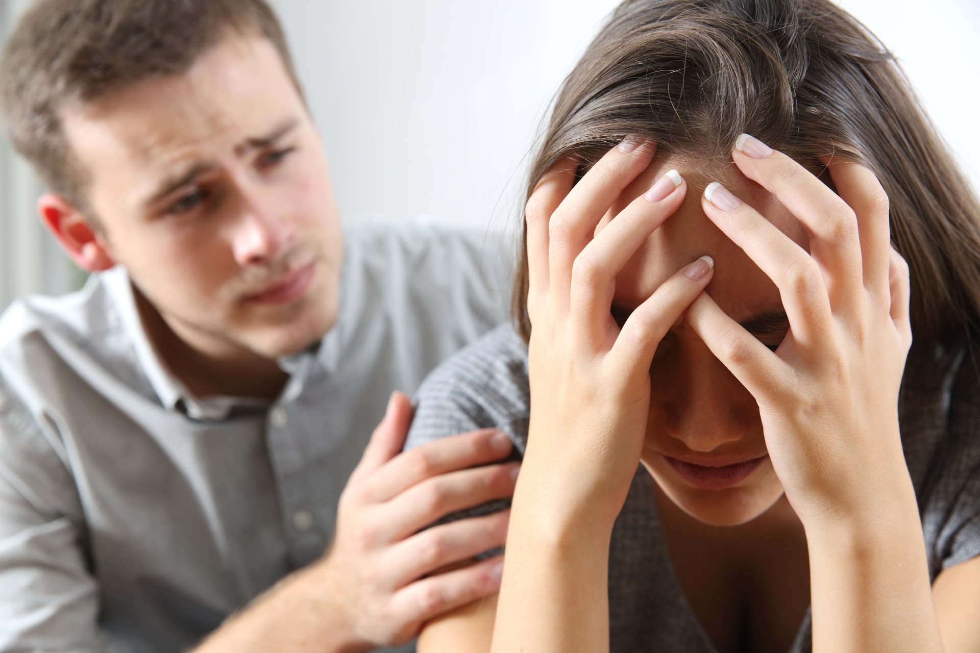 Betrayal Sensitivity A distressed woman with head in hands being comforted by husband.