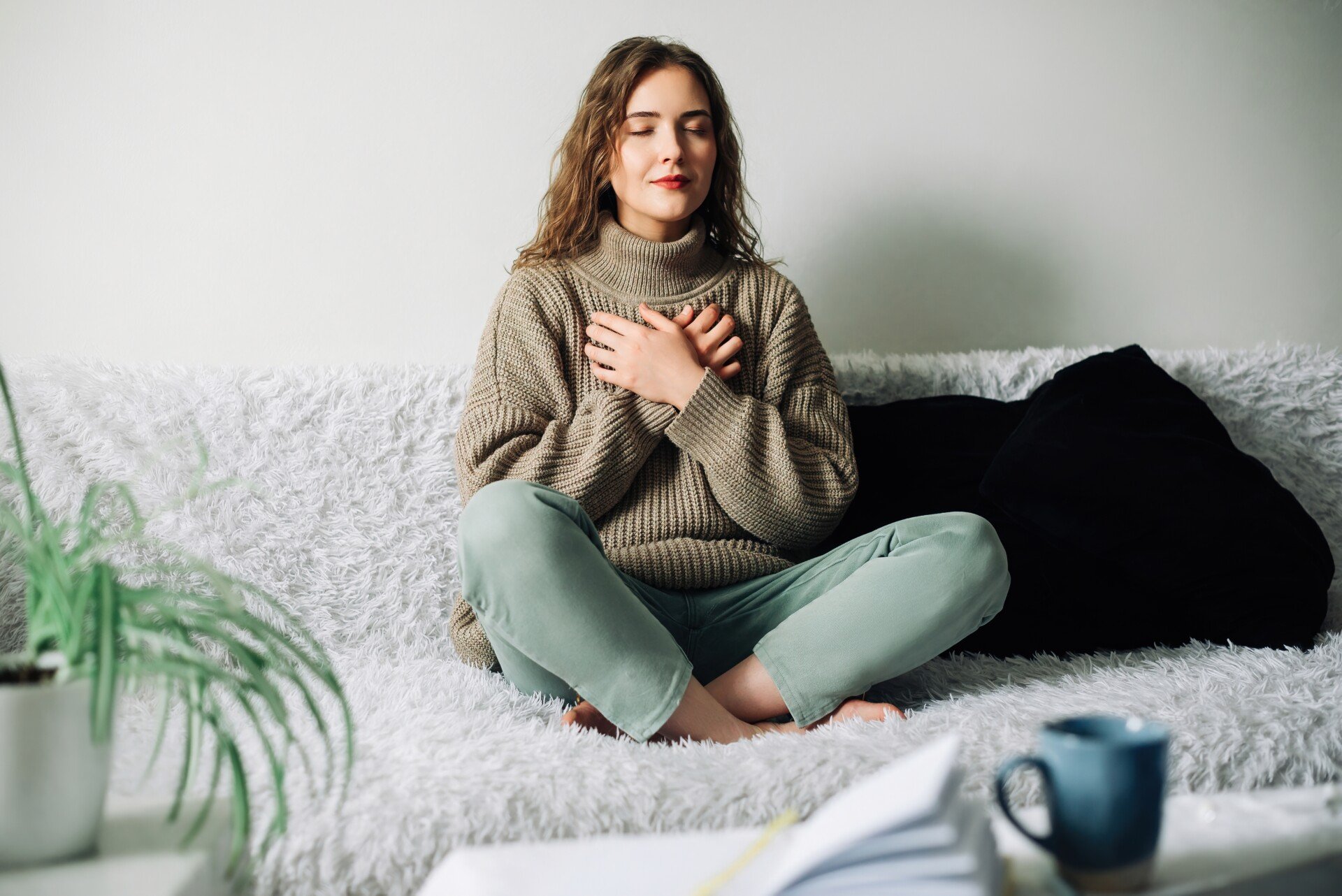 Woman sat cross-legged on the bed, hands on chest, relaxation technique.