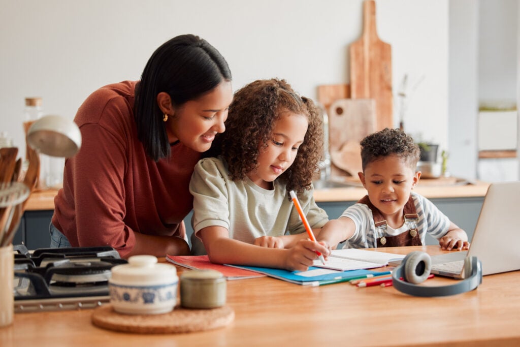 A mother helping her two children on a creative project at the kitchen table.