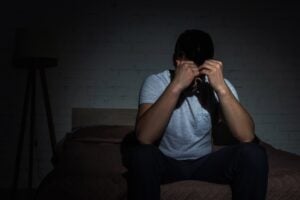 A depressed man struggling with trauma sat in a dark room, head in hands.