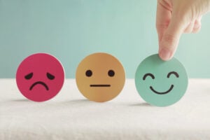3 different emotional faces with fingers picking up the happy face.