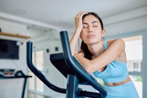 An unmotivated woman on a cross-trainer, eyes closed.