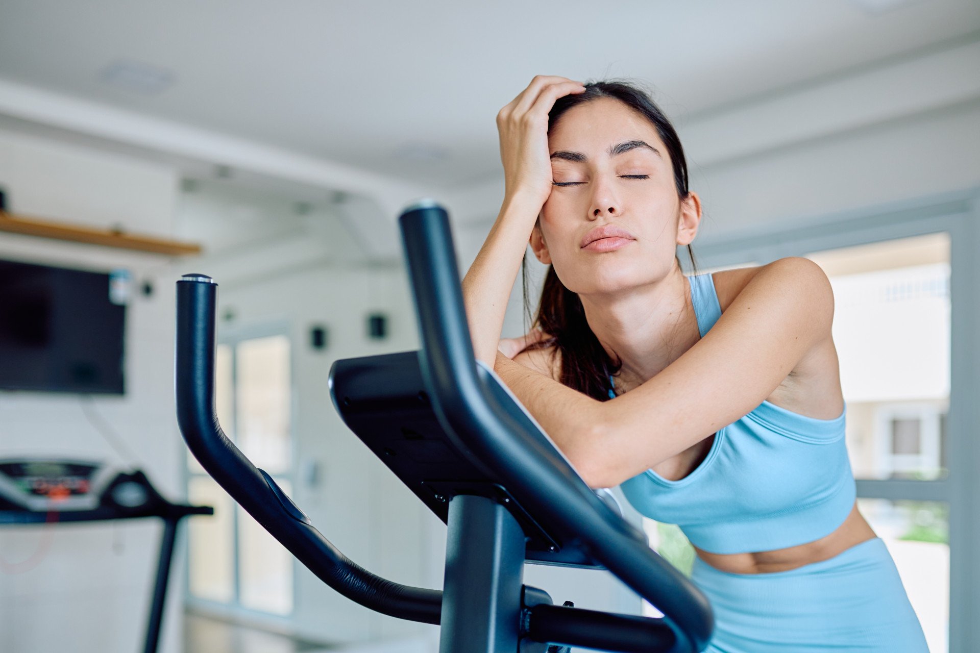 An unmotivated woman on a cross-trainer, eyes closed.