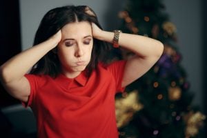 A stressed woman with hands on head, stood in front of a festive tree.