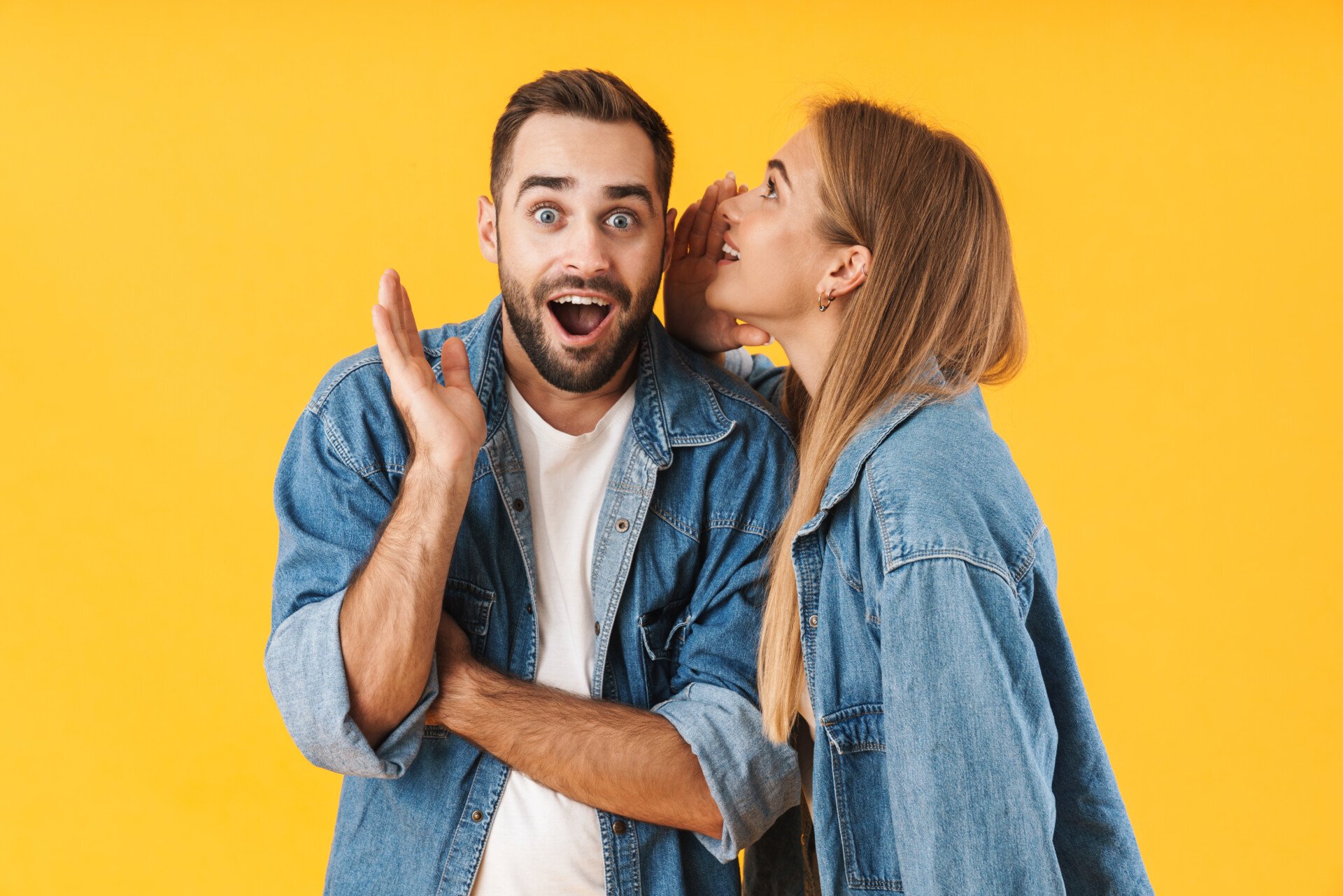 A woman whispering into a surprised man's ear