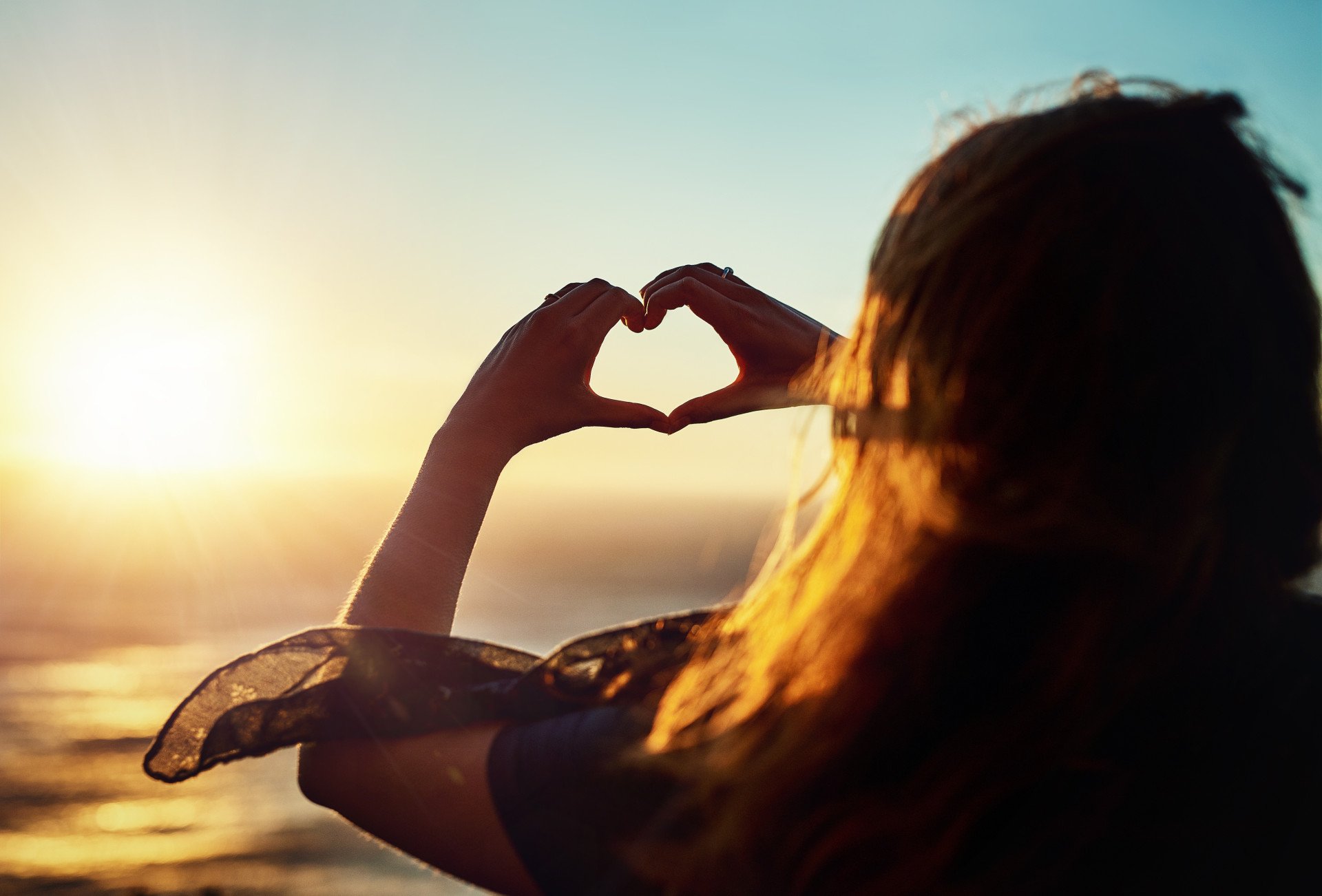 Gratitude Someone making hands into a heart shape at sunset looking at the ocean.