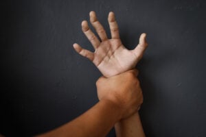 a hand grabbing another's wrist and holding it up against a black wall.
