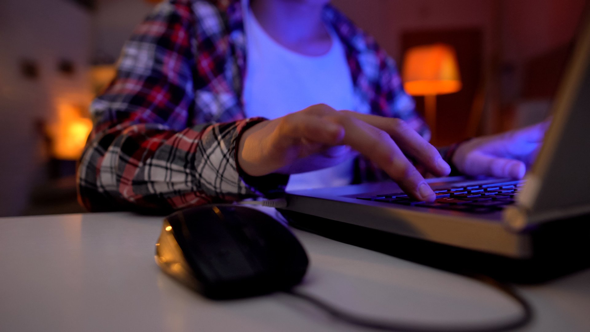 Close up of a young person typing on their laptop in a dark room.