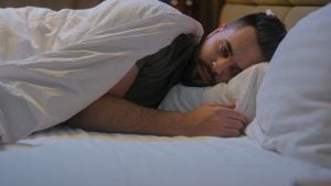 A man lay in bed overthinking, looking worried.