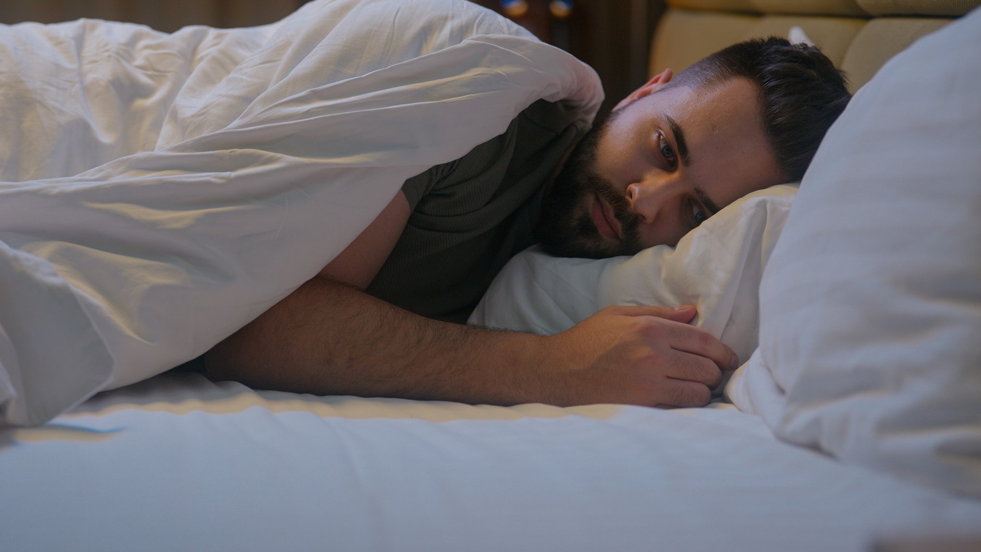 Overthinking A man lay in bed overthinking, looking worried.
