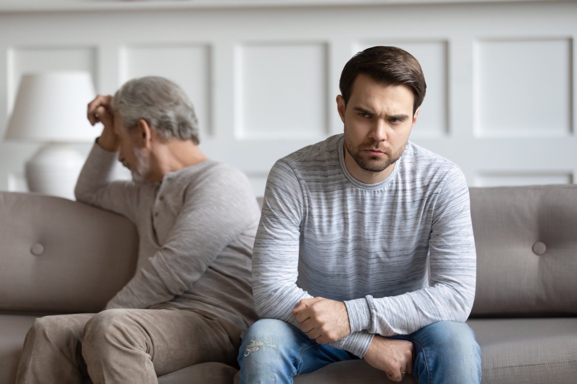 A father and his adult son sat on a sofa facing away from each other.