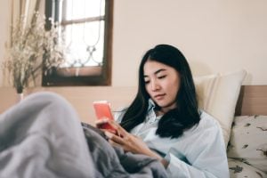 A woman lay on bed looking at phone.