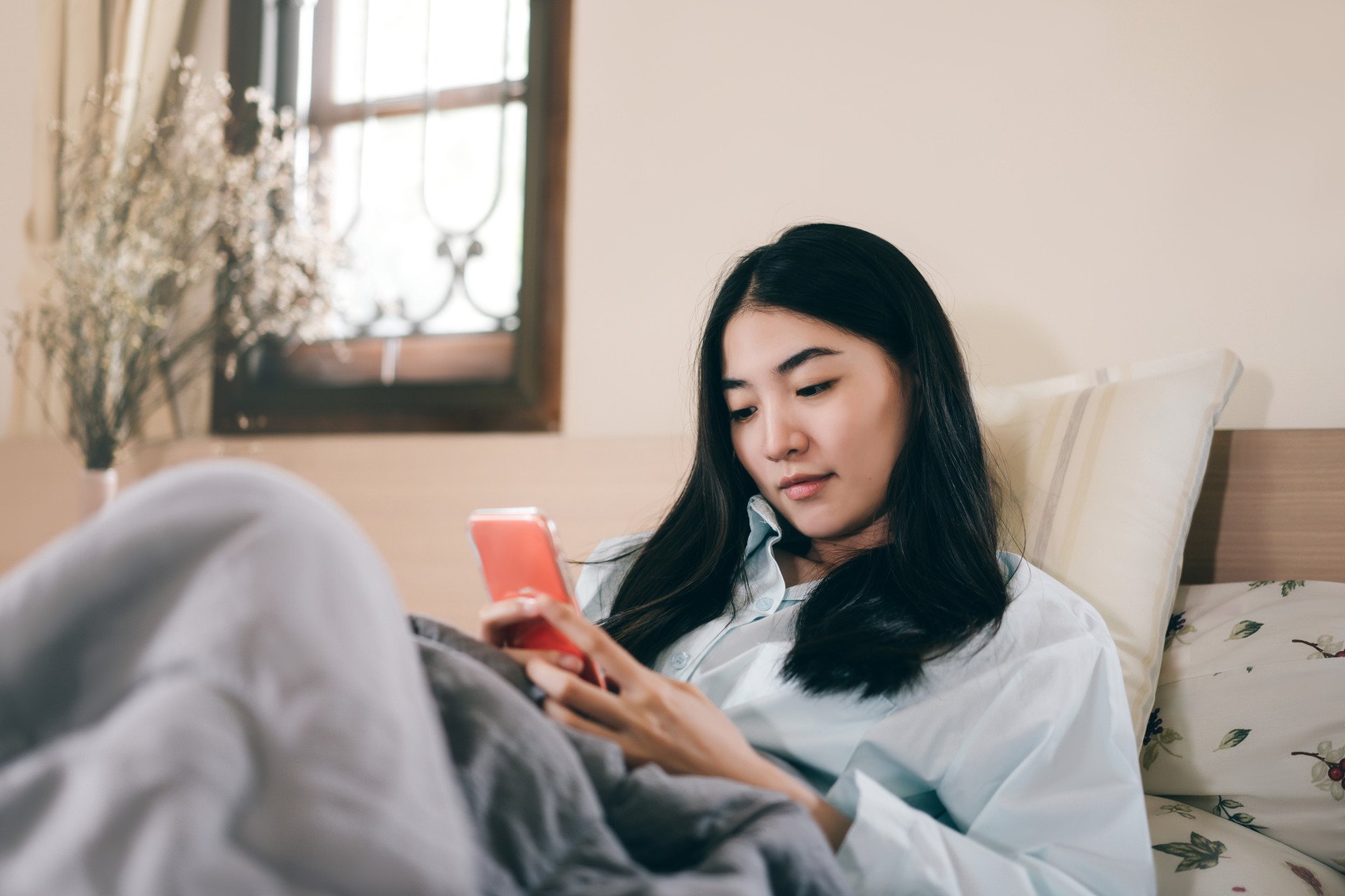 A woman lay on bed looking at phone.