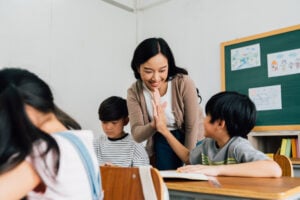 A smiling female teacher giving child in class a high five.