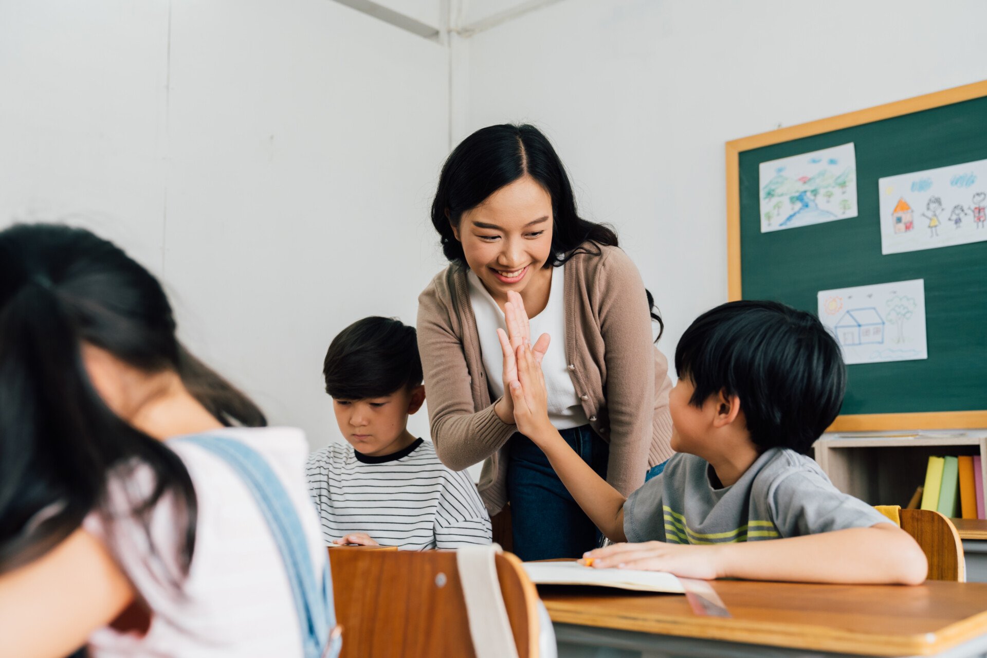 A smiling female teacher giving child in class a high five.