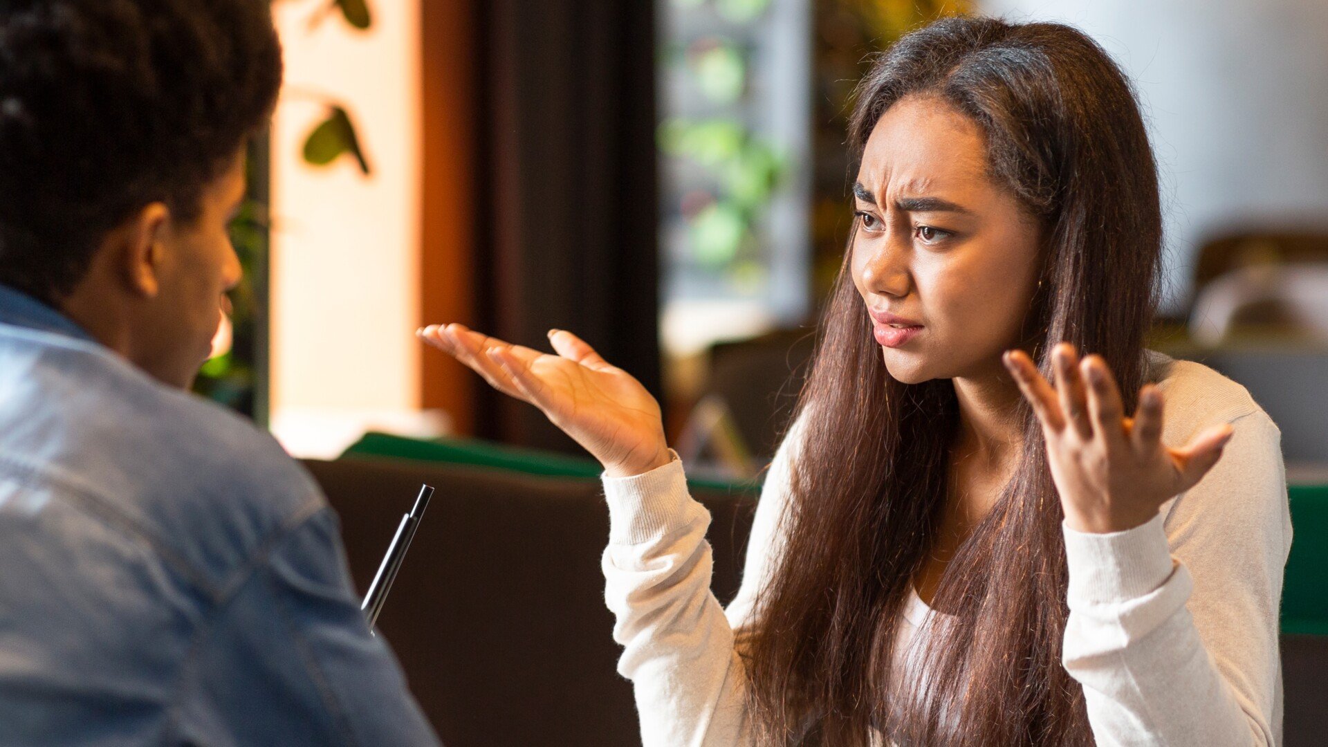 Relationship Ambivalence A couple facing each other in a restaurant with the woman holding up her hands in confusion.