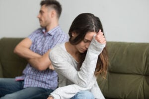 A frustrated couple facing away from each other, man has arms crossed, woman has head in hand.