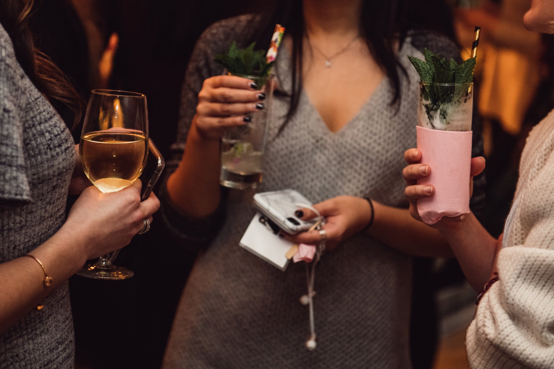 Safety Behaviors Woman socialising with a group of friends while holding a drink and her phone and headphones as a clutch.