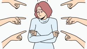 A sad woman with her arms crossed while lots of fingers point at her