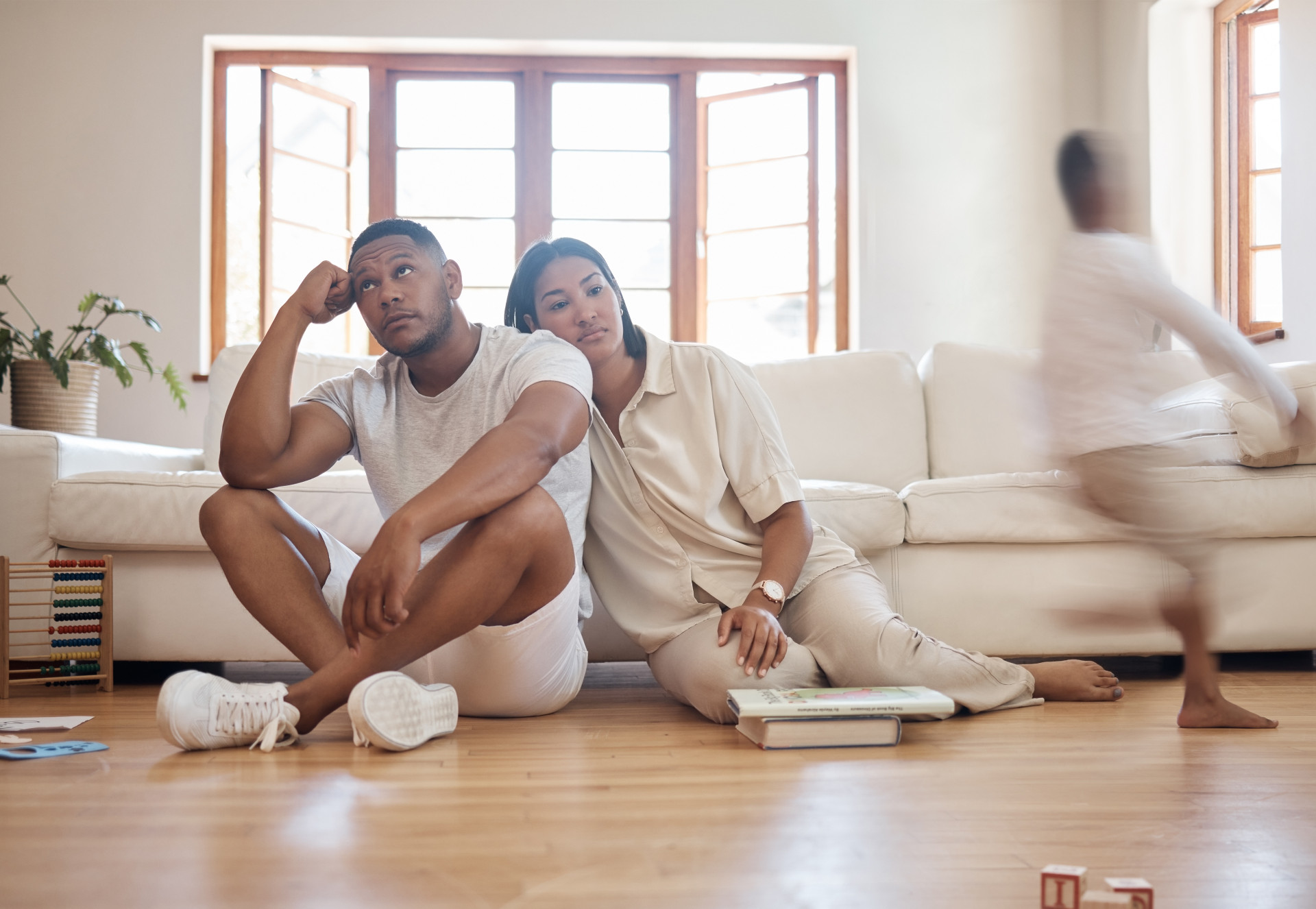 Stressed parents sat on the floor while their child is running around.