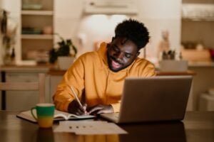 A student working at home on the laptop and writing notes.